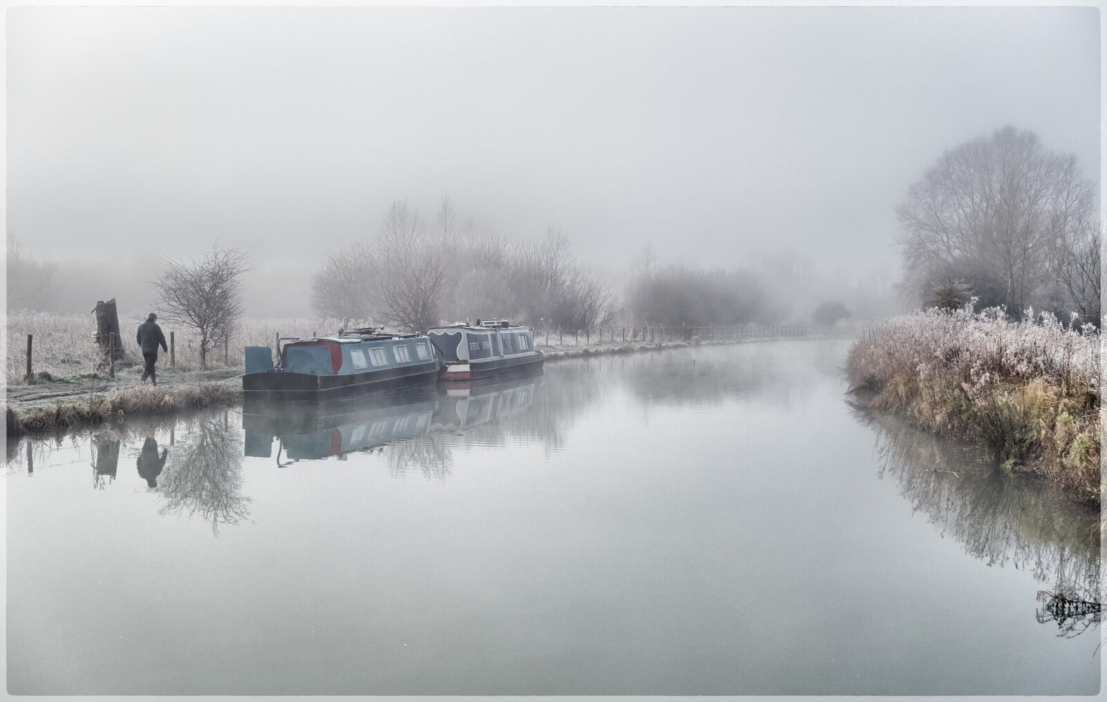 A quiet Black Country canal in early-morning mist, with narrowboats moored and two figures walking the towpath.